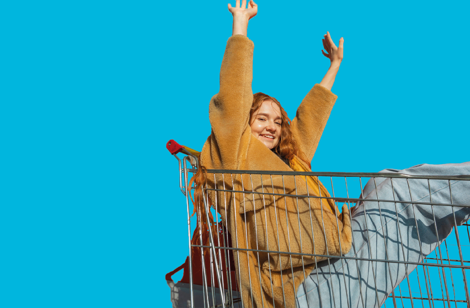 Frau sitzt fröhlich in einem Einkaufswagen vor blauem Hintergrund