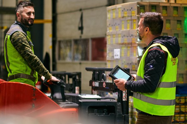 Zwei Männer mit Sicherheitswesten im Lager beladen einen LKW mit Pallette